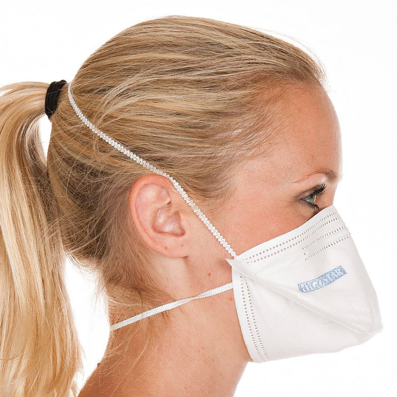 Profil einer blonden Frau mit einer weißen Schutzgesichtsmaske, gezeigt vor einem einfachen weißen Hintergrund.