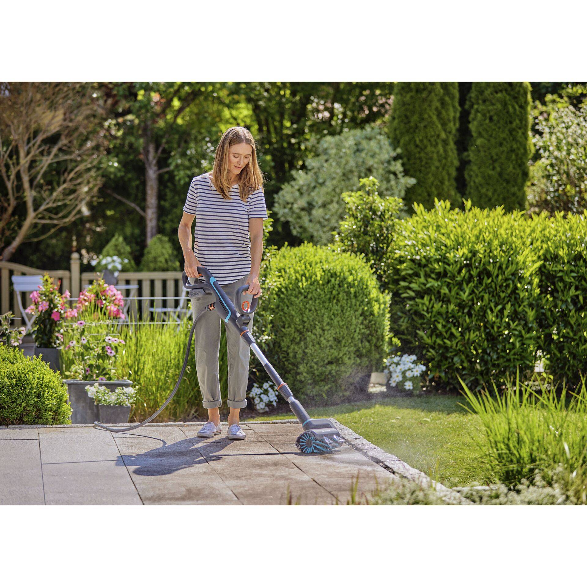 Frau, die einen tragbaren elektrischen Terrassenreiniger zum Reinigen von Steinpflaster in einem Garten verwendet