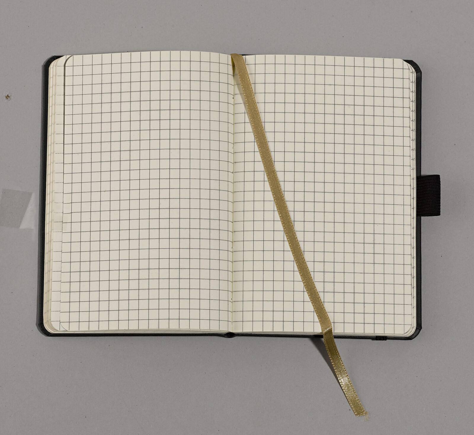 Ein offenes, gittergemustertes Notizbuch mit einem goldfarbenen Lesezeichenband auf einer grauen Oberfläche.