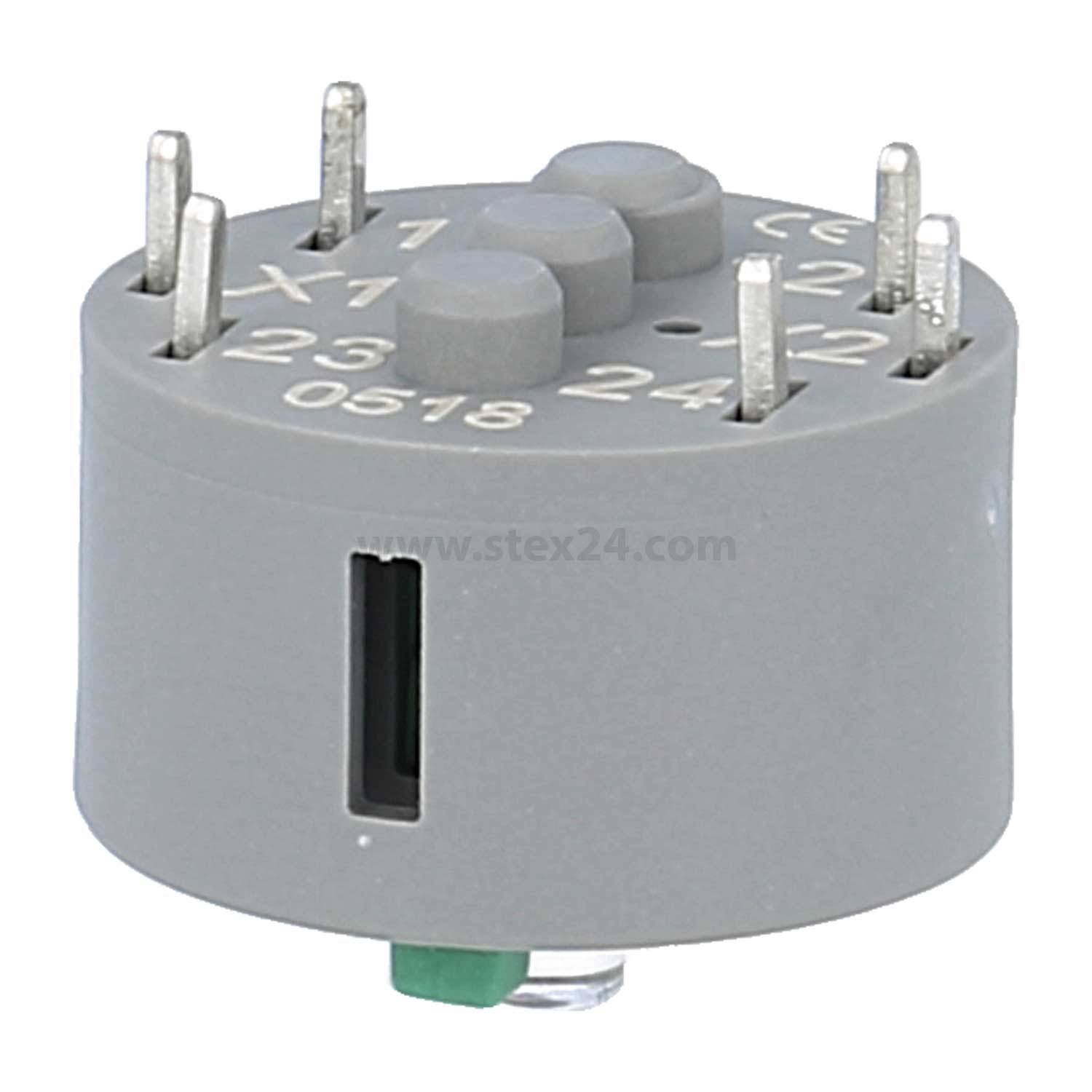 Ein zylindrisches graues Elektrobauteil mit mehreren Metallstiften, die oben herausragen, gekennzeichnet mit den Codes „X1", „23"", „24"".