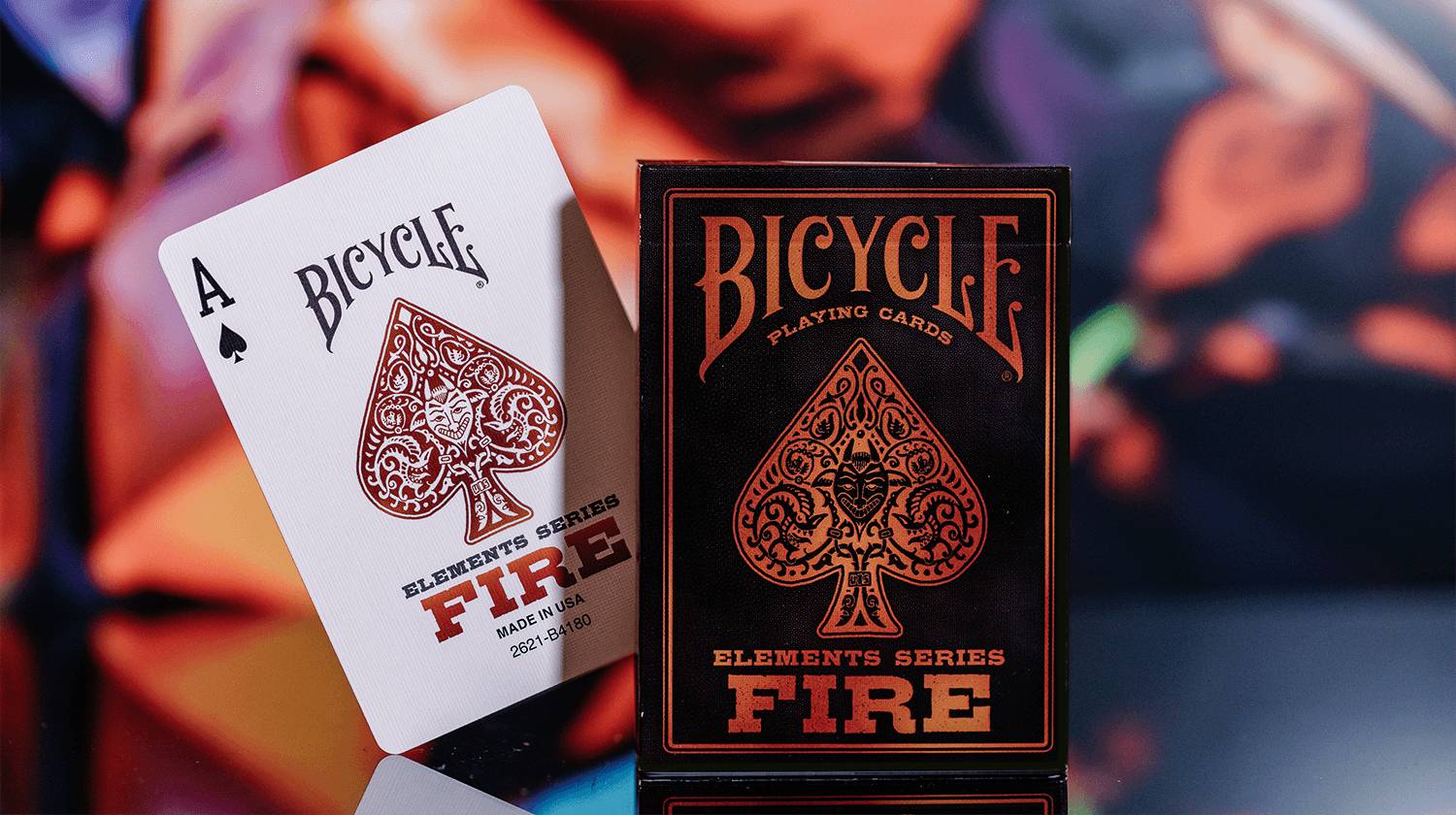 Zwei Spielkartenschachteln von Bicycle aus der Elements-Serie Feuer, eine weiße und eine schwarze mit orangenem Pik-Design, nebeneinander angezeigt.