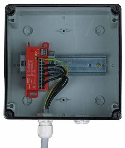 Eine graue elektrische Verteilerdose mit einem roten Klemmblock im Inneren, verbunden durch farbige Kabel. Die Dose ist auf einer Metallplatte montiert.