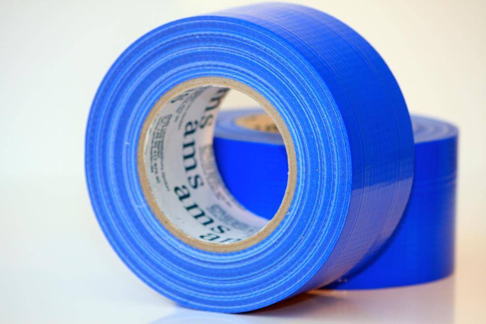 Eine Rolle leuchtend blaues Klebeband mit einer weiteren Rolle, die teilweise dahinter sichtbar ist, auf einem schlichten, hellen Hintergrund.