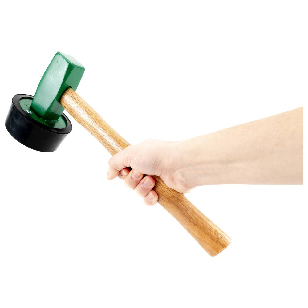 Eine Hand umfasst einen Hammer mit einem Holzgriff und einem grün, gummierten Kopf, vor einem weißen Hintergrund.