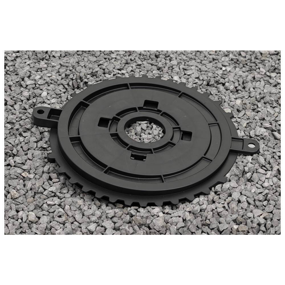 Ein rundes, schwarzes Kunststoffzahnrad mit Zähnen, das auf einer Kiesfläche liegt. Das Zahnrad hat ein zentrales Loch und mehrere kleinere Schlitze.