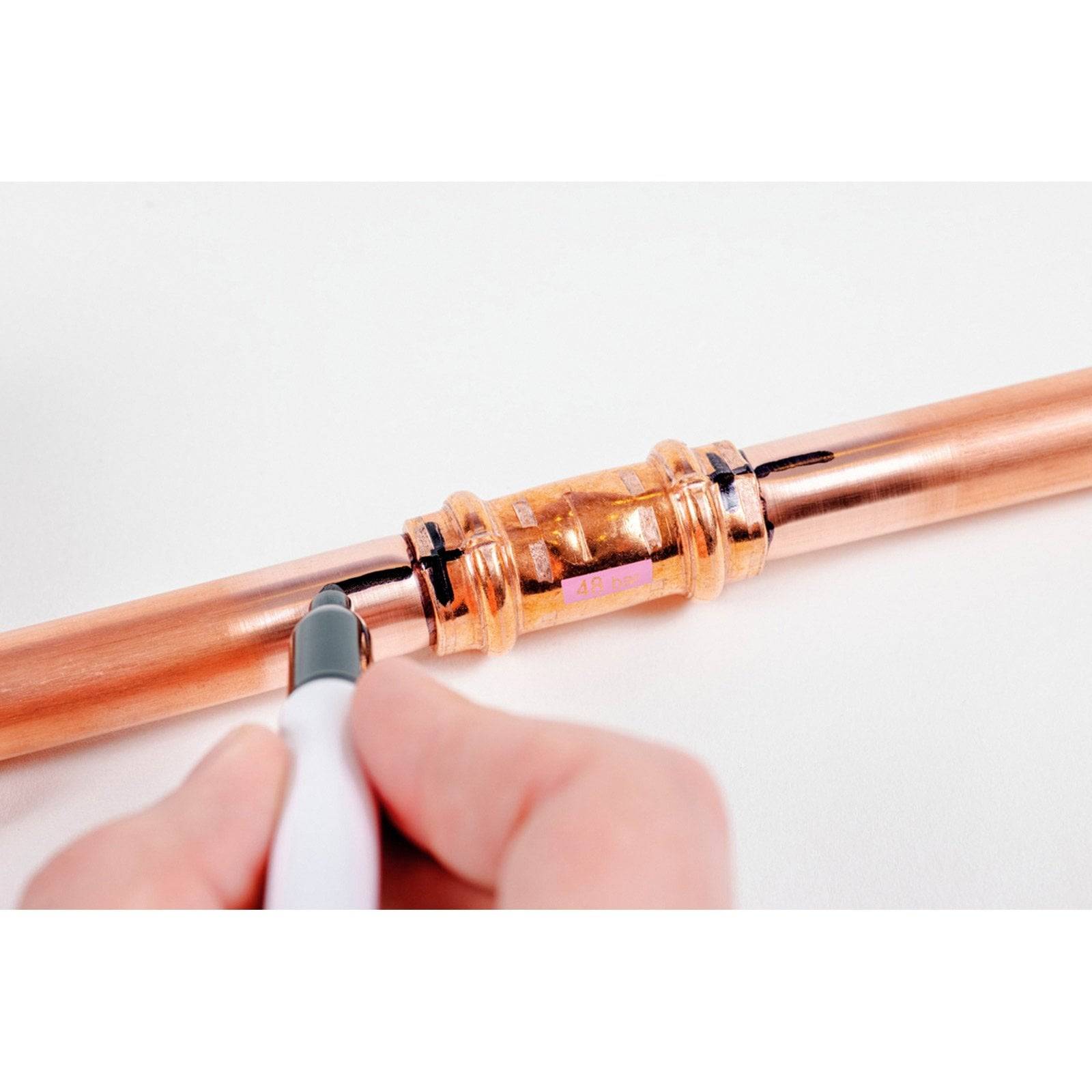 Eine Hand markiert mit einem Stift ein Kupferrohr und bereitet einen Schnitt vor. Das Rohr weist in der Mitte eine Kupplungsverbindung auf.