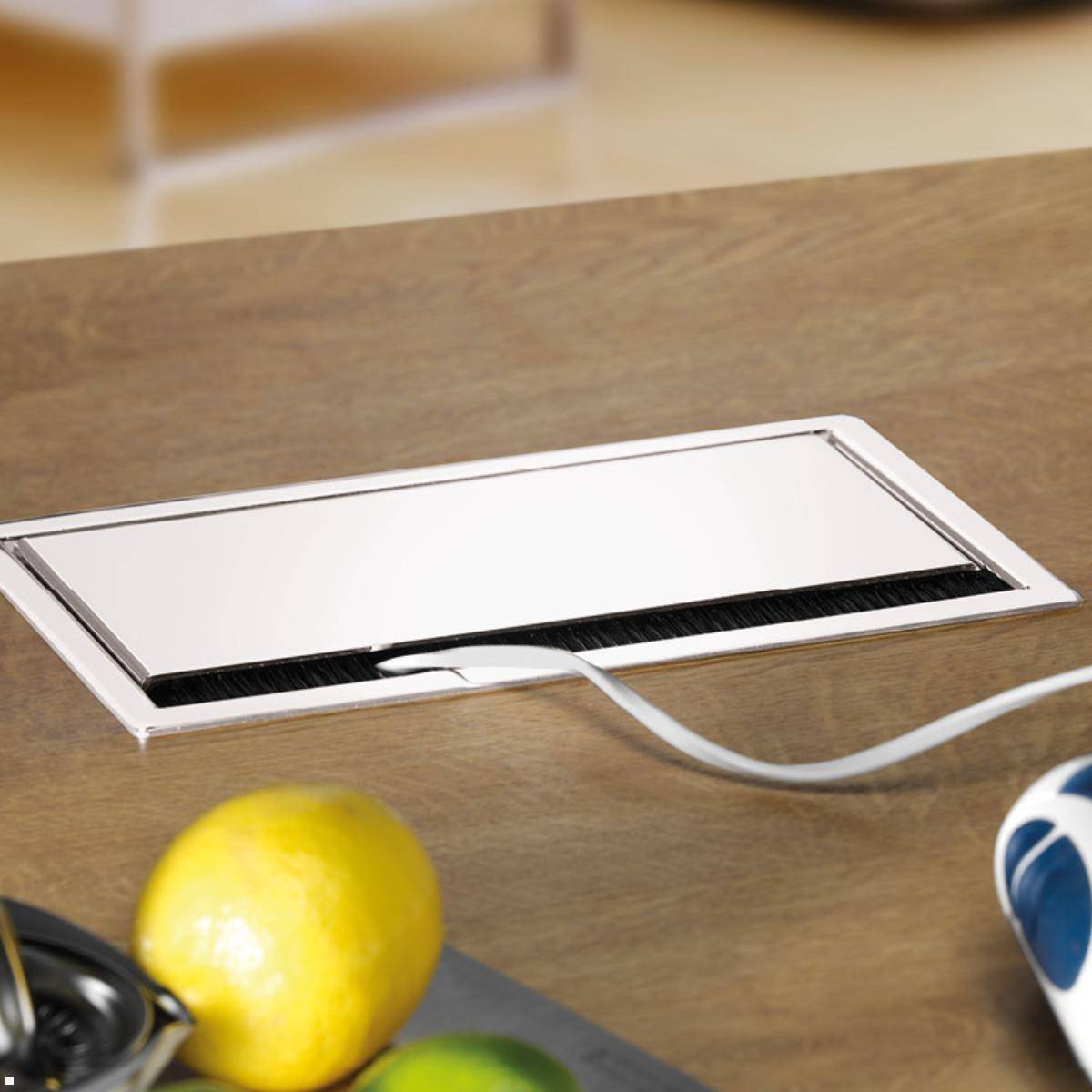 Eine Küchenarbeitsplatte mit einer geschlossenen Steckdoseneinheit zum Hochklappen, umgeben von Zitronen und Limetten im Vordergrund.