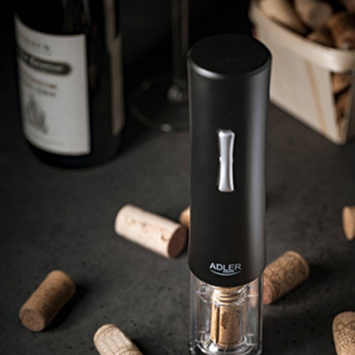 Elektrischer Weinöffner auf einer dunklen Oberfläche, umgeben von Weinkorken und einer Weinflasche, was auf eine Weinverkostung oder ein Abendessen hindeutet.