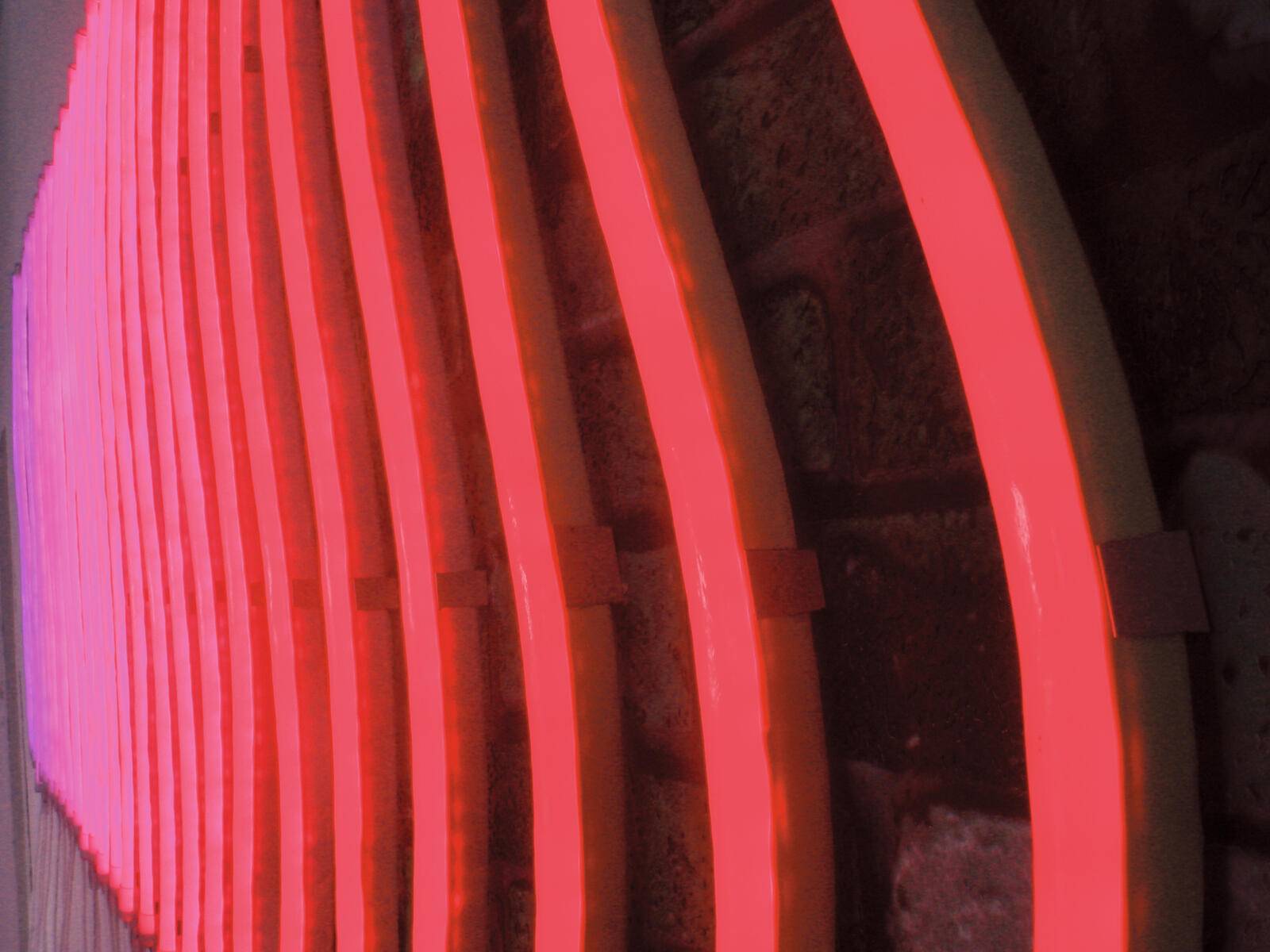 Leuchtend rote Neonlichter, die eine Serie paralleler Linien gegen eine dunkle, strukturierte Wand bilden.