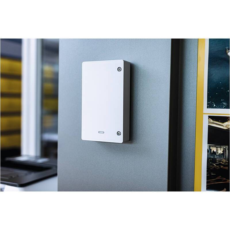 Weiße wandmontierte elektrische Schaltanlage auf einem grauen Paneel in einer industriellen oder Büroumgebung.