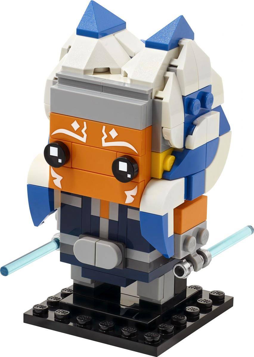 LEGO-ähnliche Modell-Minifigur aus Bausteinen einer blauen, weißen und orangefarbenen maskierten Figur, die zwei hellblaue Schwerter auf einem schwarzen Sockel hält.