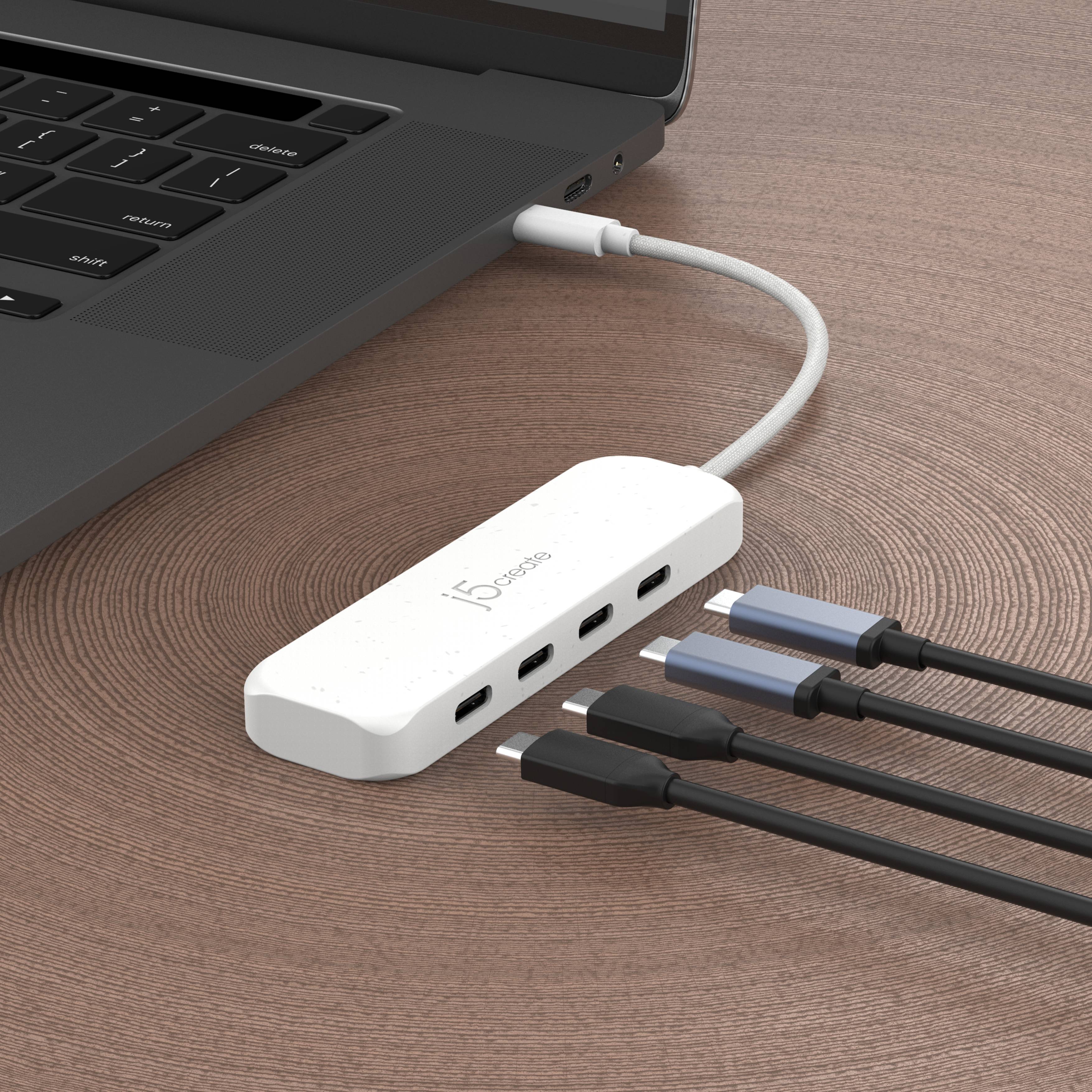 Laptop verbunden mit einem weißen USB-C-Hub mit vier eingesteckten USB-A-Kabeln auf einem Holzschreibtisch.