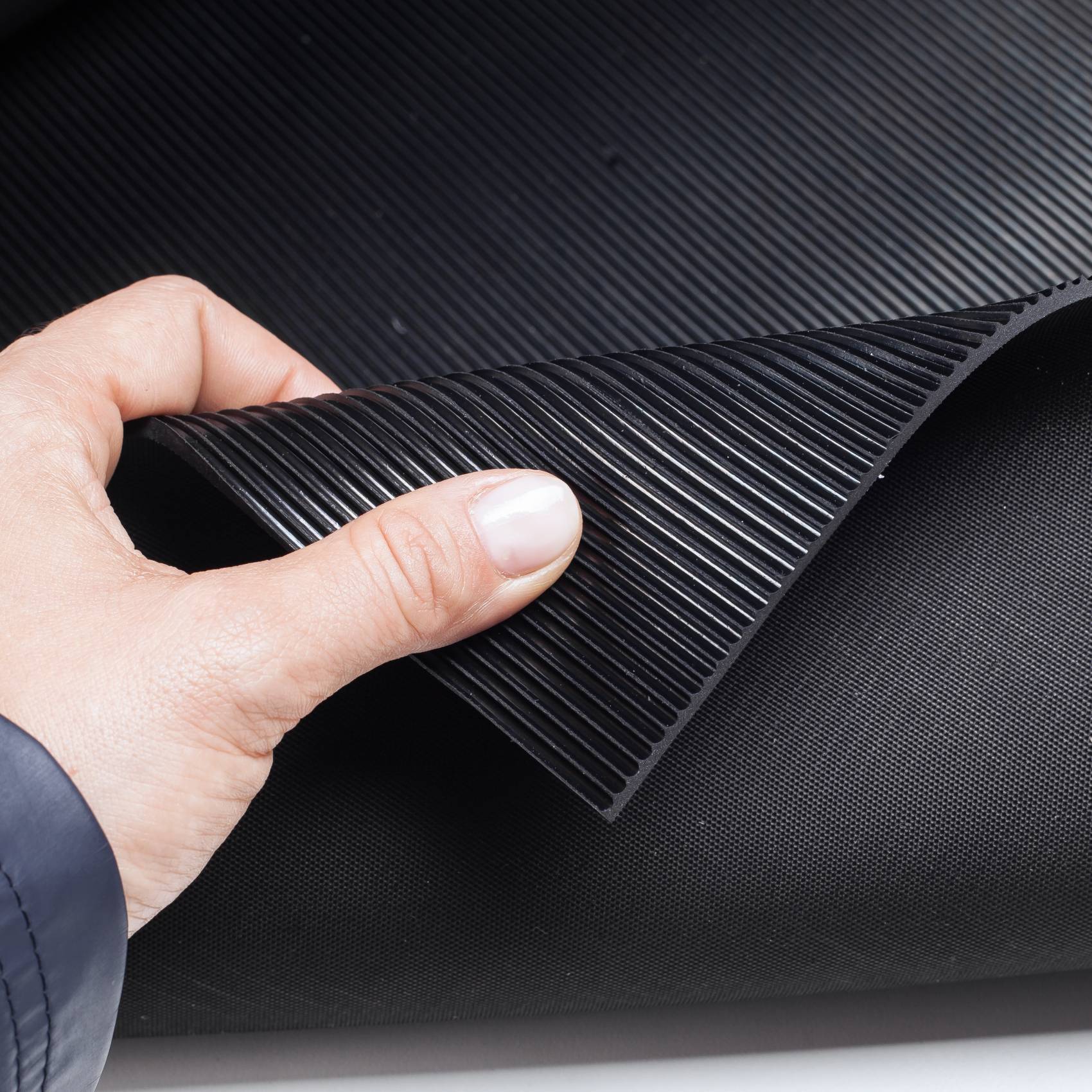 Hand hebt eine flexible schwarze gerippte Matte oder Folie an und zeigt ihre strukturierte, biegbare Oberfläche.
