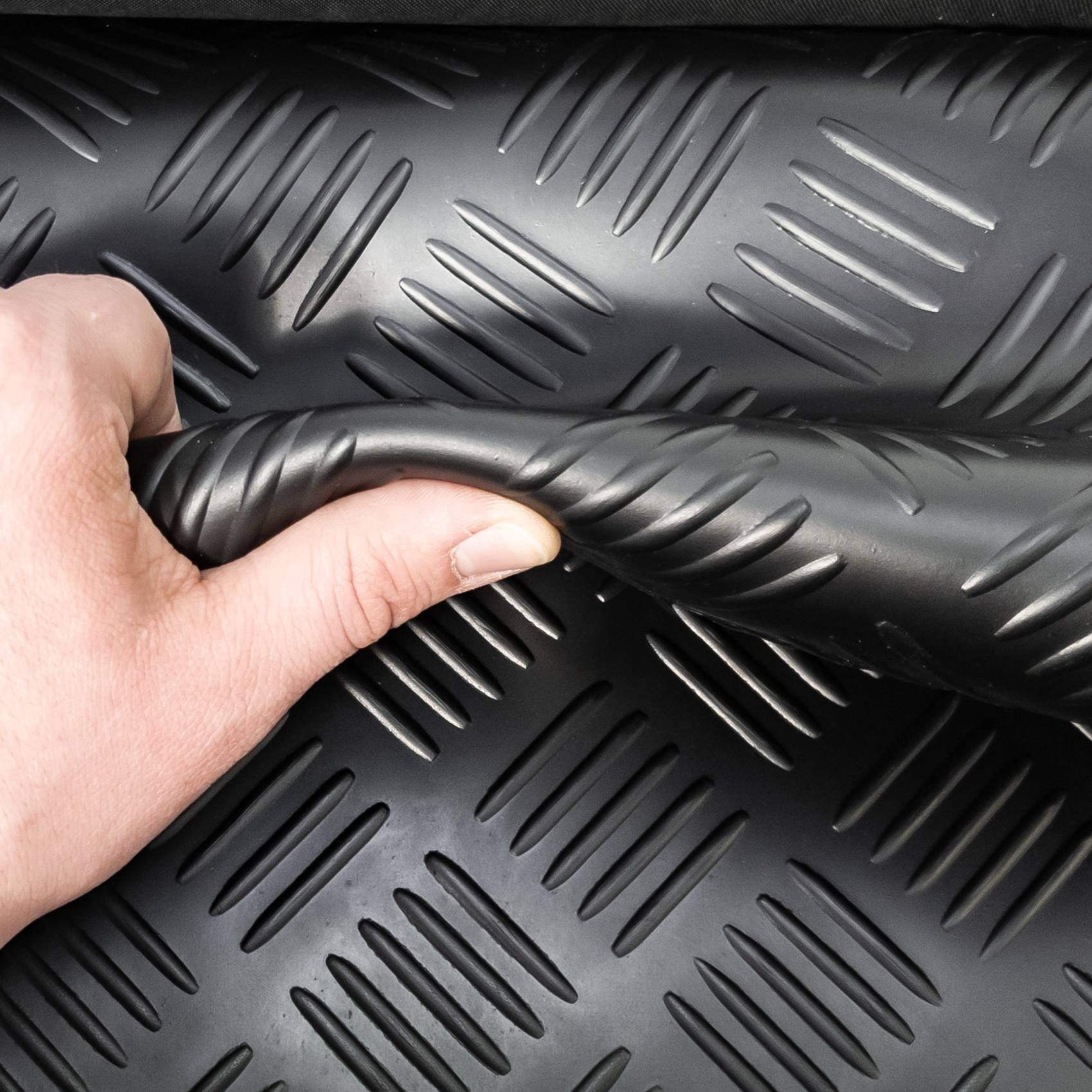 Nahaufnahme einer Hand, die eine schwarze strukturierte Gummimatte mit erhabenen diagonalen Rippen biegt, die ihre Flexibilität und Oberflächenmuster zeigt.
