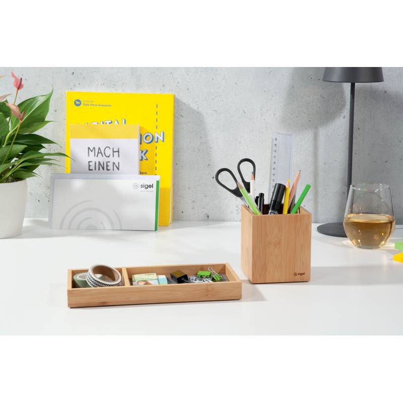 Ein aufgeräumter Arbeitsplatz mit einer Pflanze, Schreibwaren und einem Glas Weißwein. Ein Schild mit der Aufschrift 