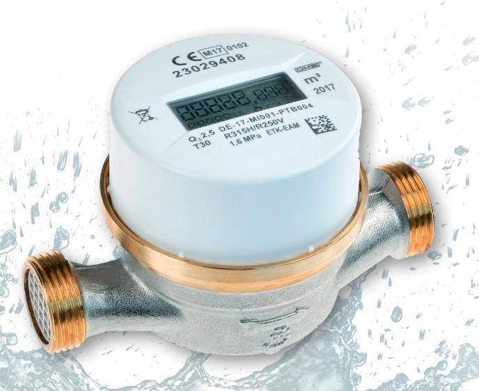 Nahaufnahme eines Wasserzählers mit Messinggewinde-Rohranschlüssen, mit digitalem Display und gedruckten technischen Markierungen.