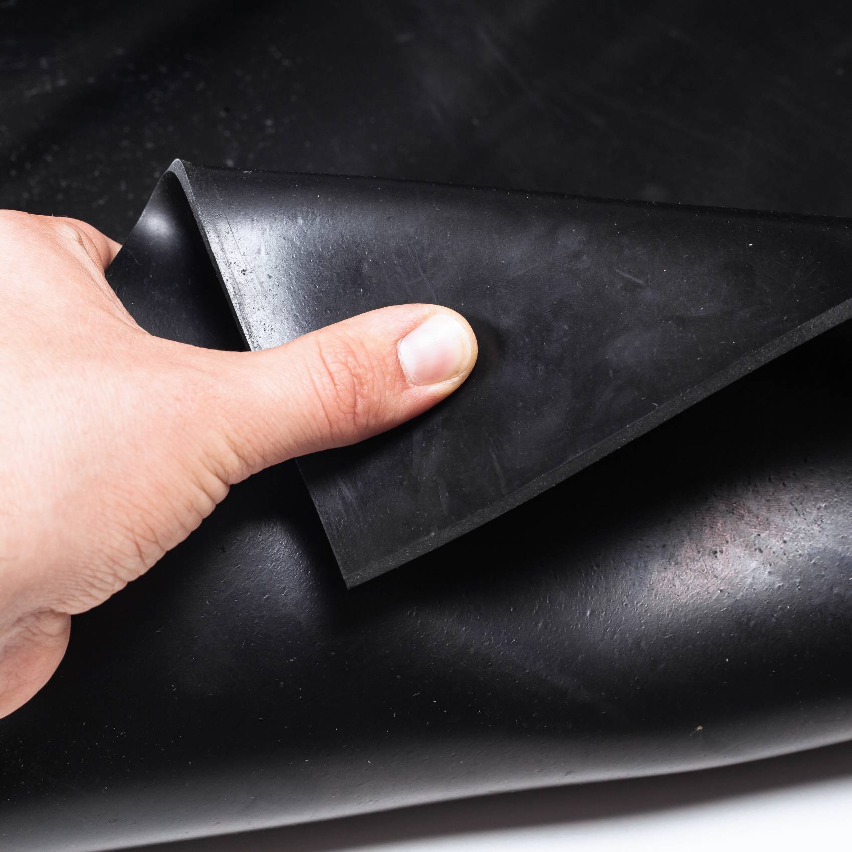 Hand hebt eine gefaltete Ecke eines schwarzen Gummi- oder Vinylblatts an, um seine flexible, matte Oberfläche zu zeigen.