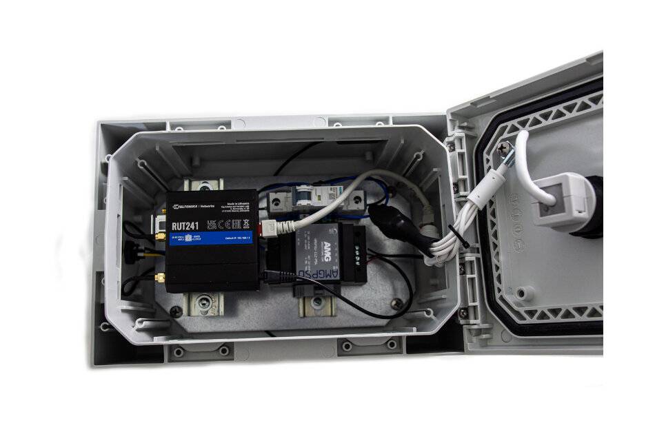 Offene elektrische Schaltschrank mit zwei montierten Netzwerkgeräten und angeschlossenen Kabeln an der Innenseite eines angelscharnieren grauen Gehäuses.