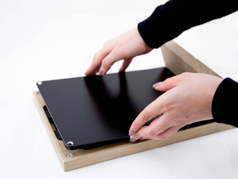 Hände, die ein schwarzes Panel von einer Holzbasis anheben, was einen Montage- oder Demontagevorgang andeutet.