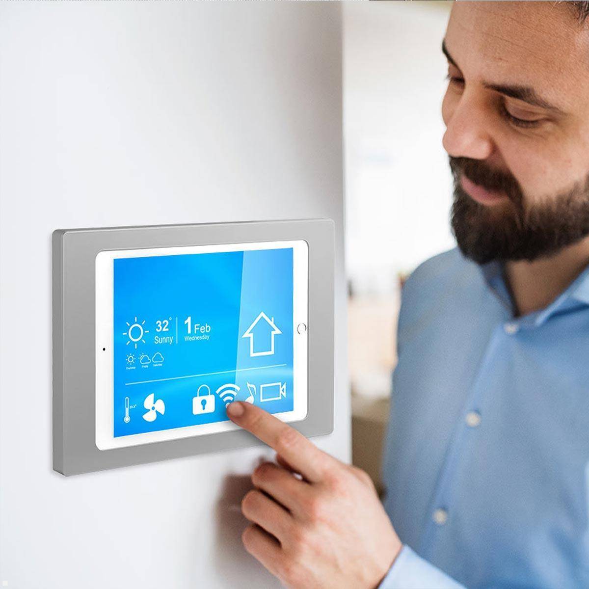 Eine Person justiert einen Smart-Thermostat, der an einer Wand montiert ist und Wetterinformationen, Temperatureinstellungen und ein Hausicon anzeigt.