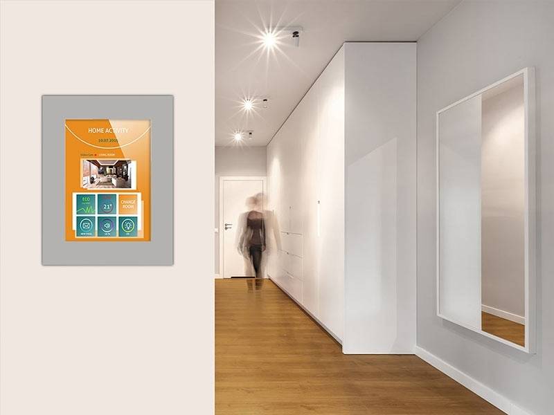 Ein moderner Flur mit Holzboden führt zu einer Türöffnung. Ein an der Wand montierter Bildschirm zeigt eine 'Home Activity'-Benutzeroberfläche mit Symbolen.