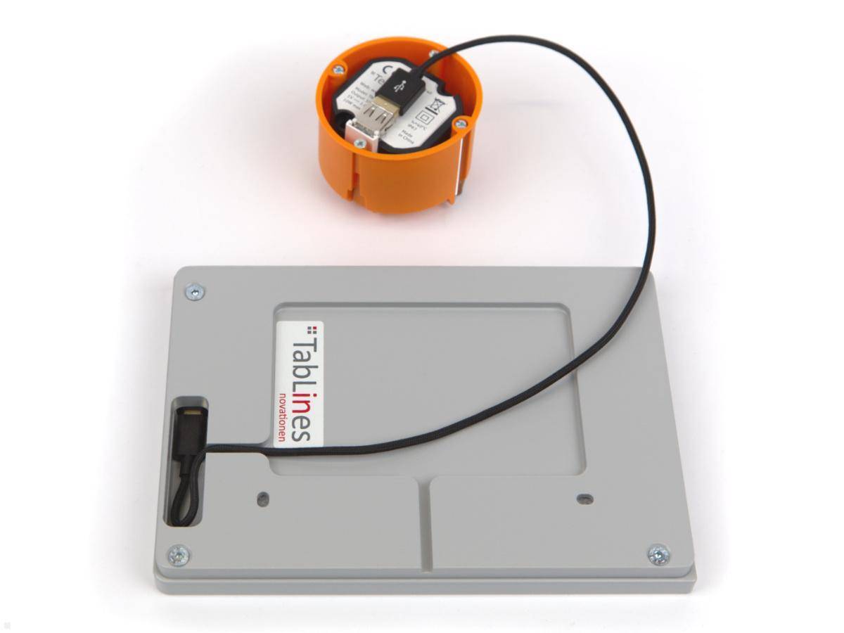 Ein an der Wand montiertes Gerät mit einem grauen Gehäuse, beschriftet mit 'Tablines'. Es ist über ein Kabel mit einer orangefarbenen kreisförmigen Steckdosenabdeckung verbunden.