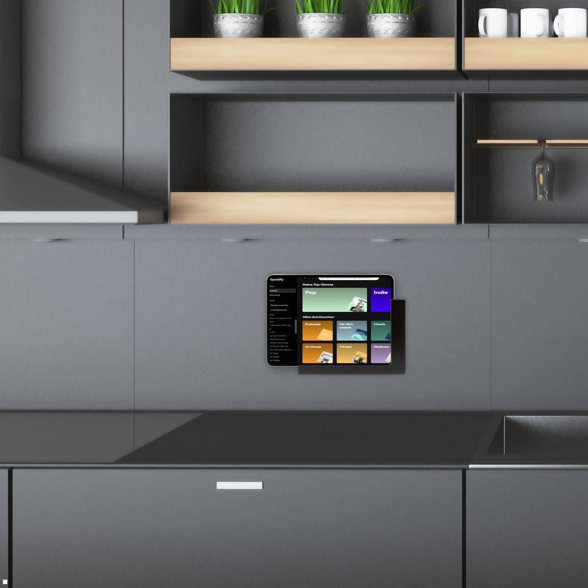 Eine moderne Küche mit dunklen Schränken und einer eleganten Arbeitsplatte zeigt ein an der Wand montiertes Tablet, das verschiedene Multimedia-Apps präsentiert.