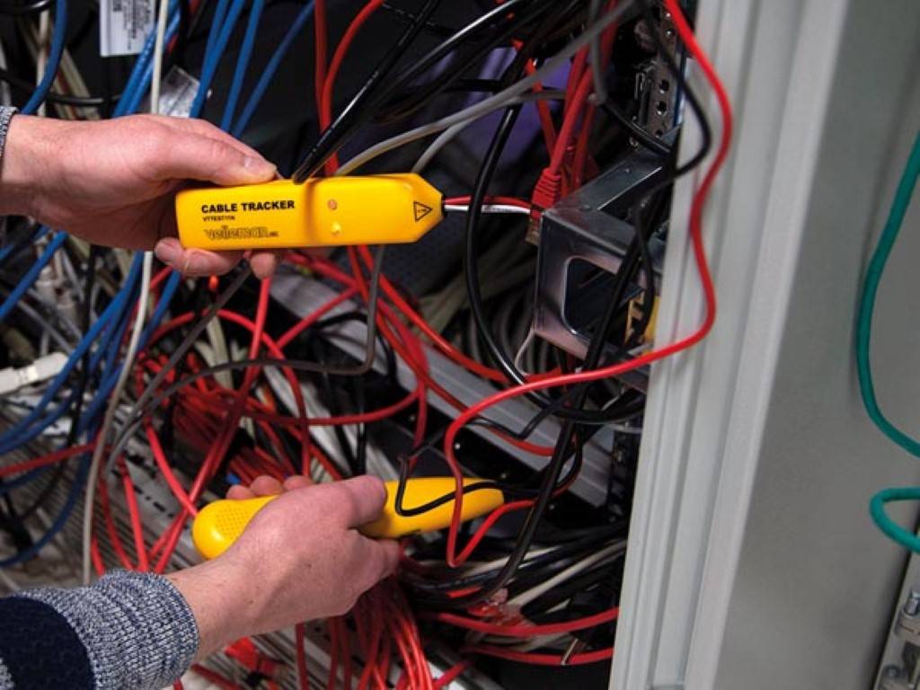 Eine Person nutzt ein gelbes Kabelsucher-Werkzeug zwischen verwirrten Drähten in einem Schaltschrank, um Verbindungen und die Verdrahtungsorganisation zu überprüfen.