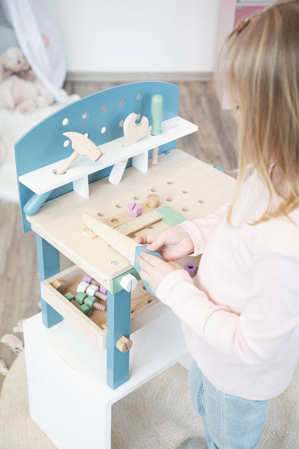 Kind spielt mit einer blauen und hölzernen Spielwerkbank, ordnet bunte Bausteine und hölzerne Werkzeuge an.