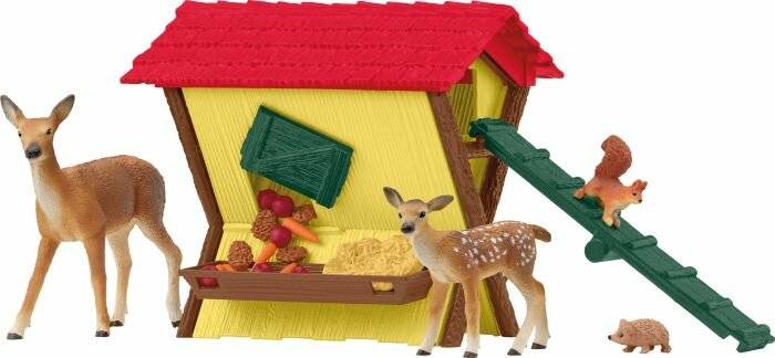 Spielzeugtierfiguren um eine gelbe Scheune mit rotem Dach, darunter ein Hirsch bei der Futterkrippe, ein Kitz auf einer Rampe, ein Eichhörnchen und ein kleiner Igel.