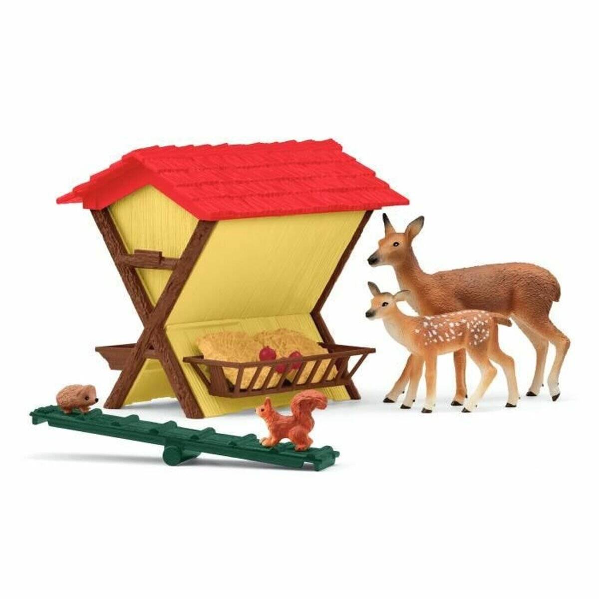 Spielzeug-Hirschfamilie neben einem kleinen Heuautomaten mit rotem Dach, mit zwei Kitzen, einer erwachsenen Ricke und kleinen Tierfiguren auf einer grünen Bahn.