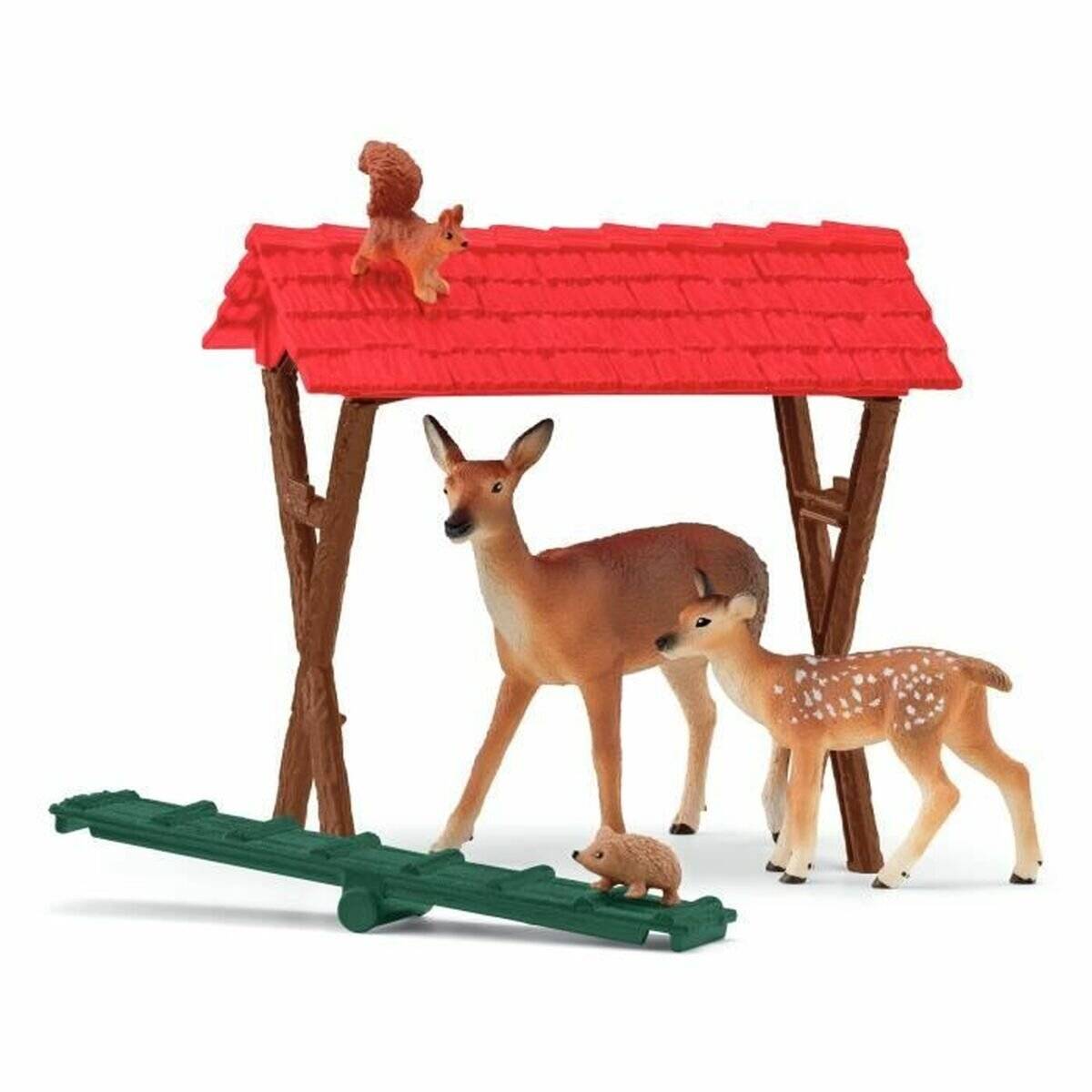 Spielzeug-Hirschfamilie unter einem rotgedeckten Unterstand, mit einem Eichhörnchen oben darauf, einer kleinen Maus darunter und einem grünen Zaun davor.