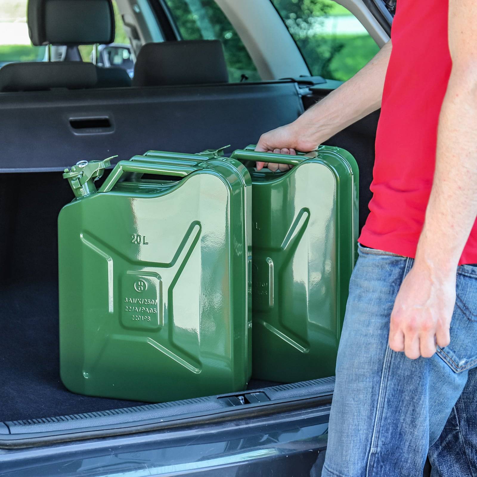 Eine Person in einem roten Shirt platziert zwei grüne 20-Liter-Kanister in den Hinterwagen eines Fahrzeugs.