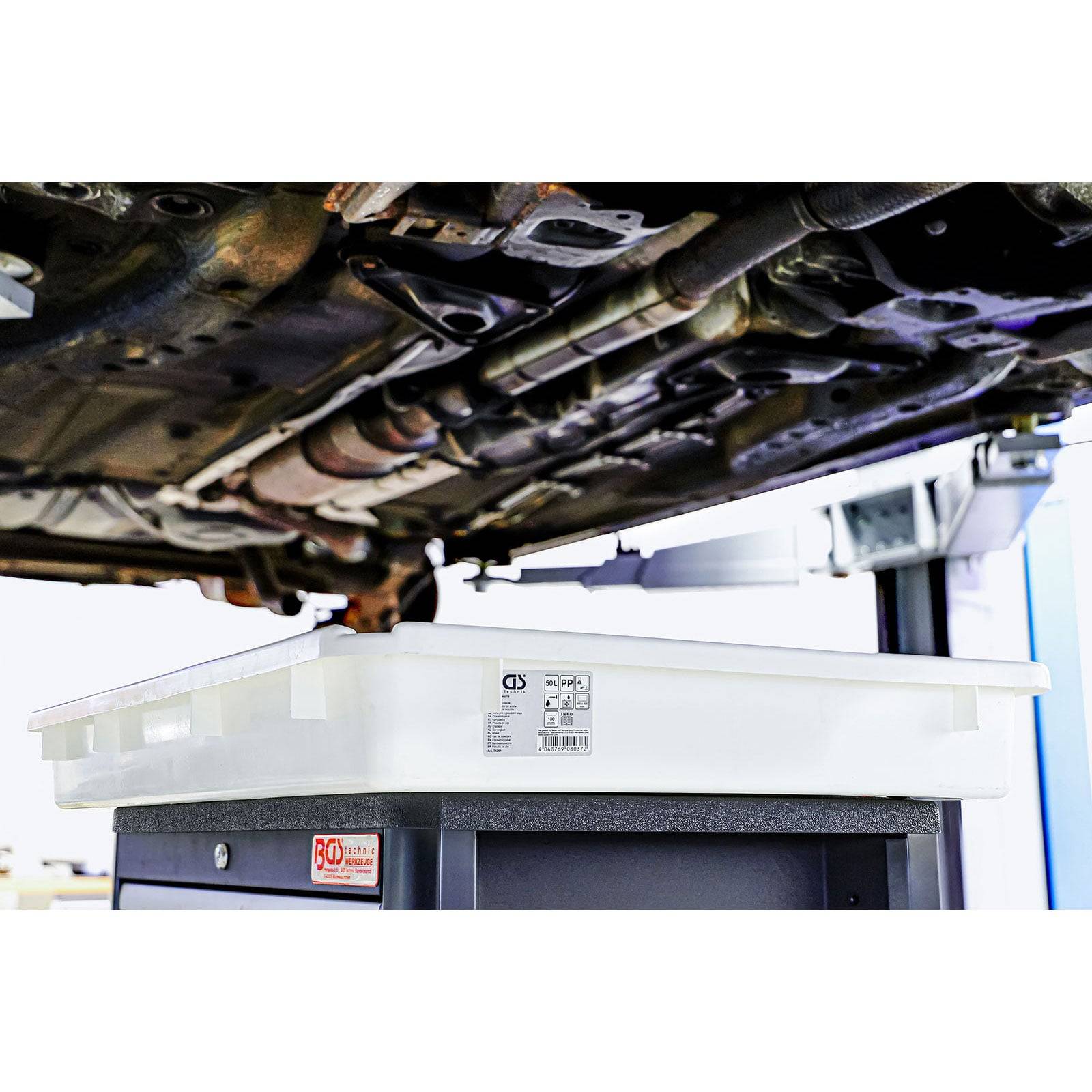 Ein Ölauffangbehälter, der unter einem auf einer Hebebühne angehobenen Fahrzeug in einer Autoreparaturwerkstatt positioniert ist und bereit ist, auslaufendes Öl während der Wartung aufzufangen.