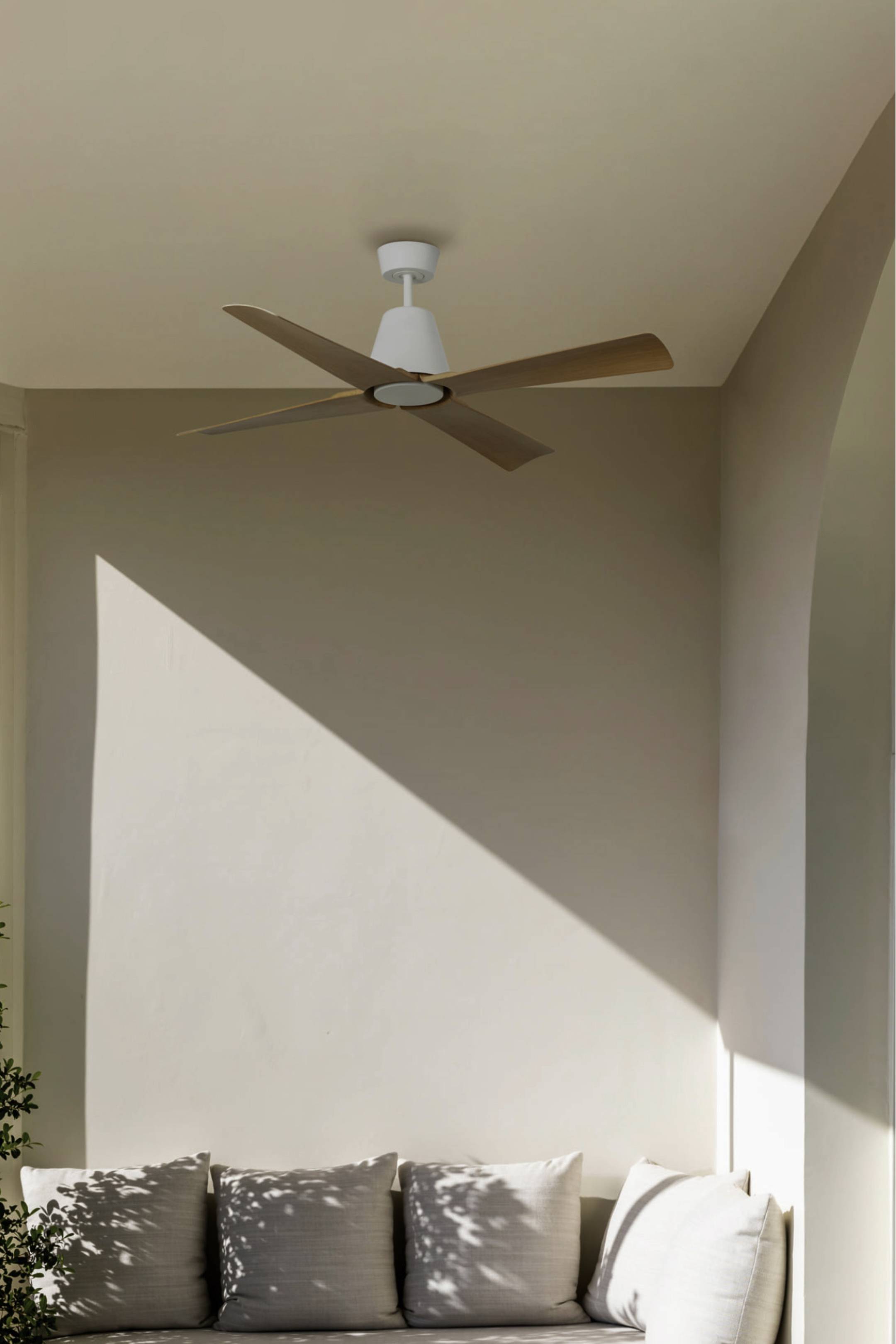 Moderne Wohnzimmerecke mit beigen Wänden, einem Deckenventilator, hellem Sonnenlicht, das einen diagonalen Schatten wirft, und grauen Kissen auf einem niedrigen Sofa.