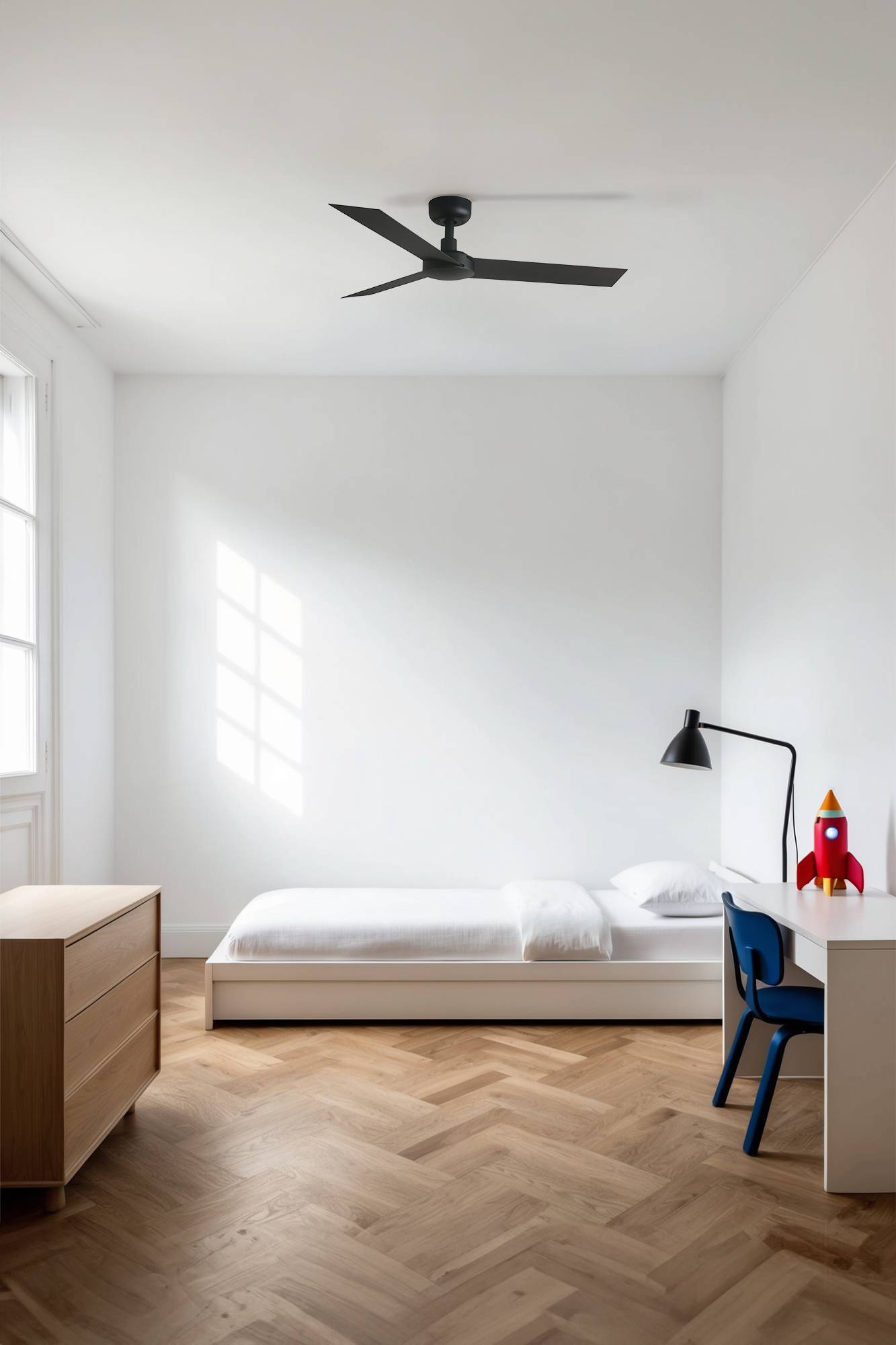 Minimalistisches Schlafzimmer mit einem Einzelbett, Schreibtisch und Stuhl, Kommode, Deckenventilator und einer kleinen Spielzeugrakete auf dem Schreibtisch neben dem Fenster.