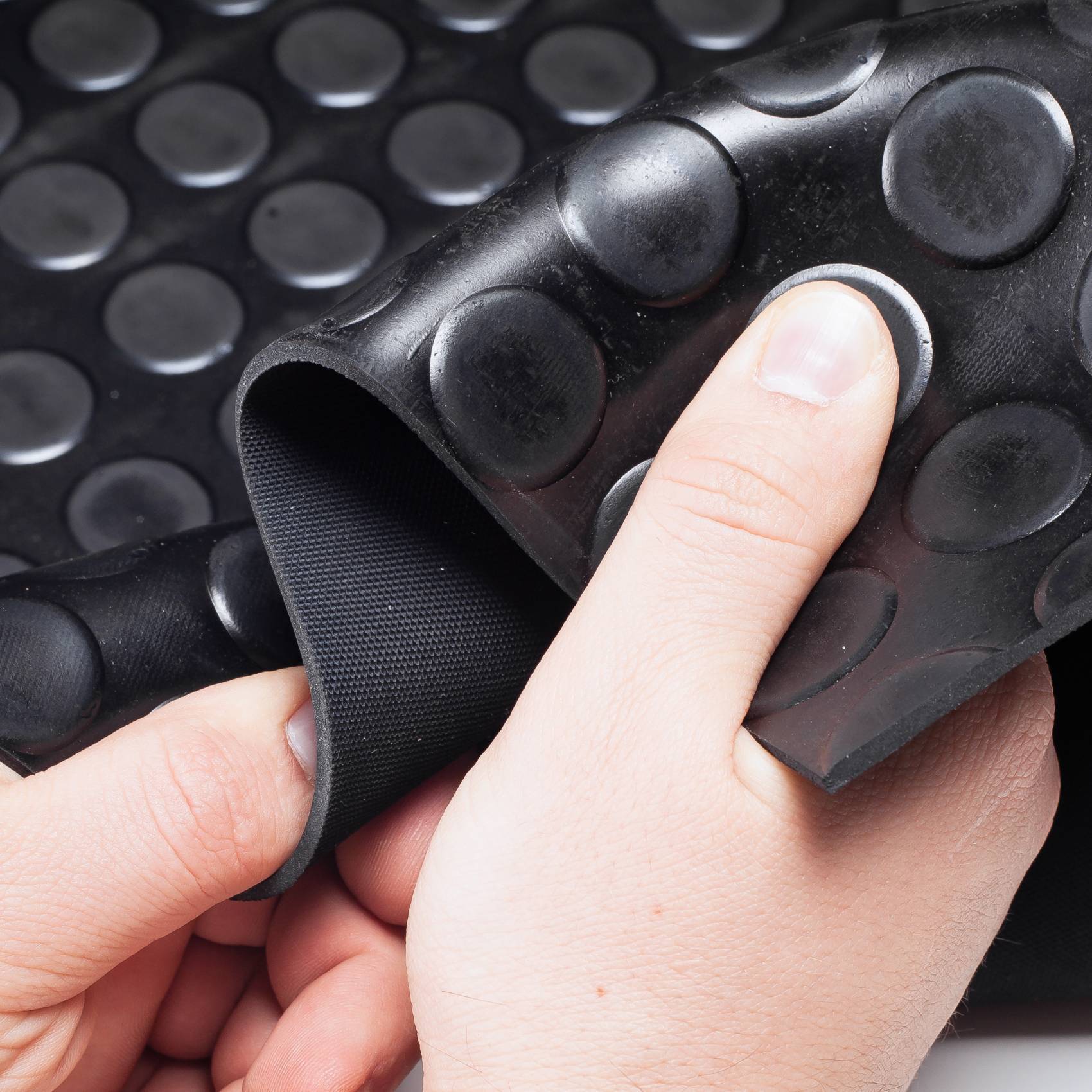 Hände, die eine schwarze Gummimatte mit erhabenen kreisförmigen Noppen zurückziehen und ihre flexible Unterseite offenlegen.