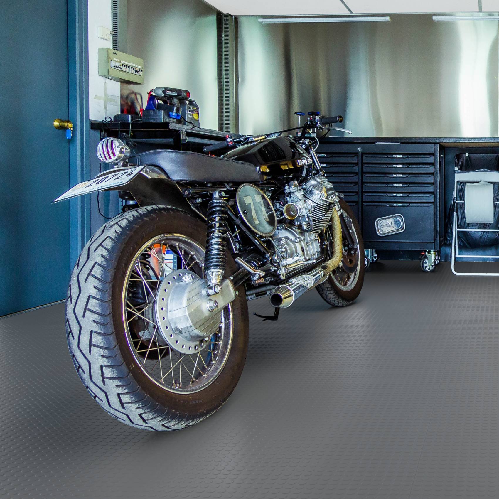 Benutzerdefiniertes schwarzes Café-Racer-Motorrad, das in einer Garage neben Werkzeugschränken und Werkstattausrüstung geparkt ist.