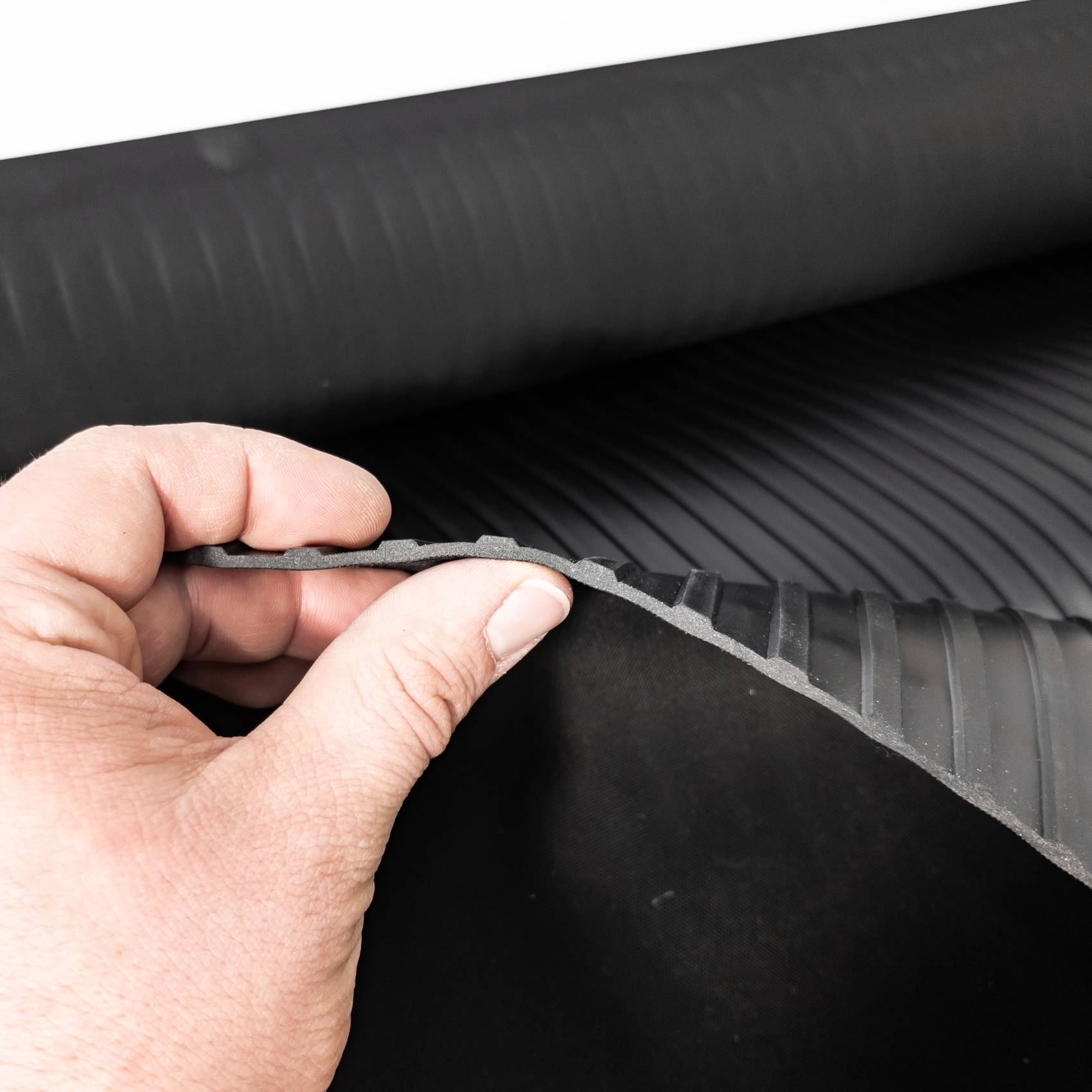 Hand, die eine flexible schwarze gerippte Matte oder ein Blatt hebt, zeigt dessen strukturierte Kante und Unterseite.