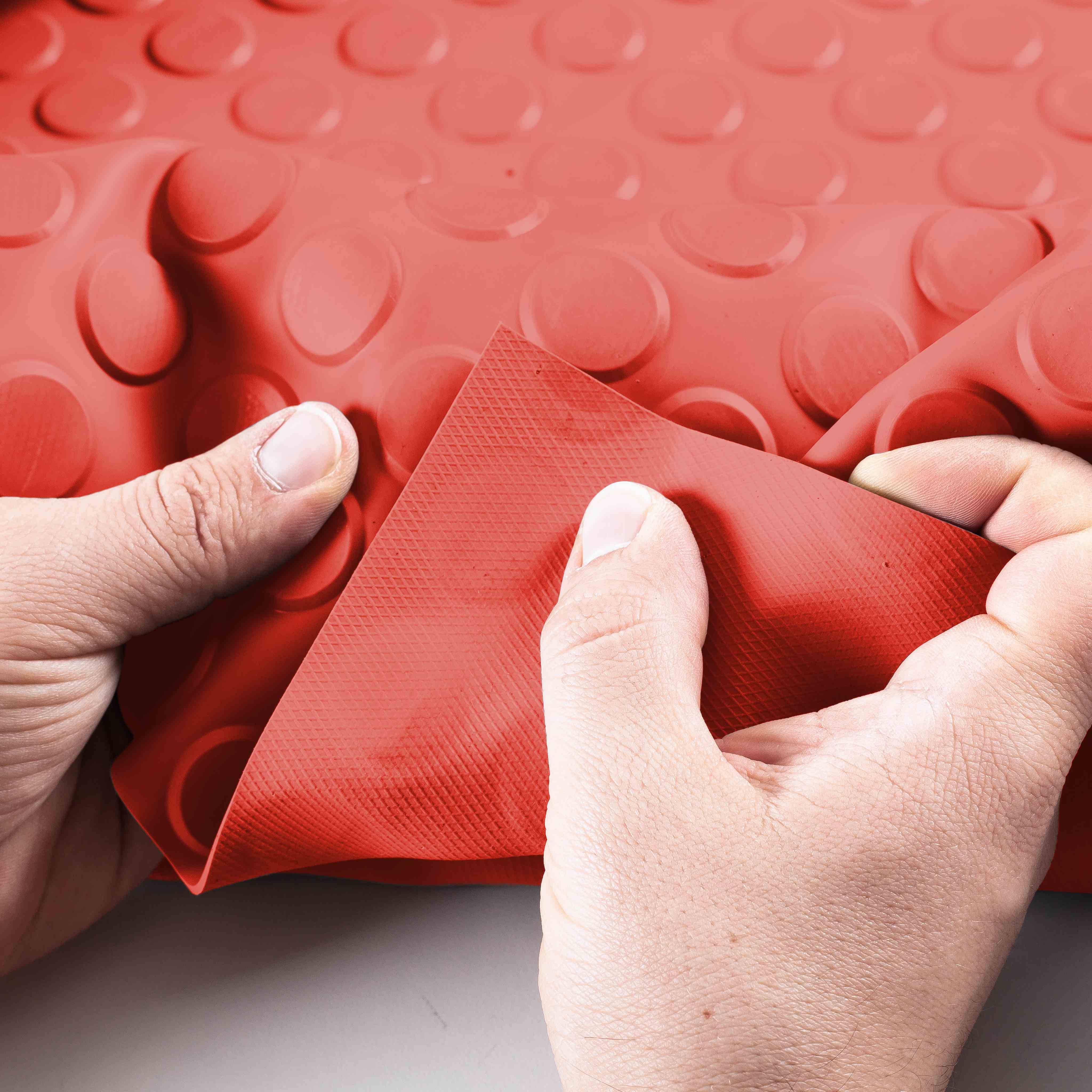 Hände, die ein rotes strukturiertes Material zurückschälen, um eine darunter liegende dunkelrote Gummifläche freizulegen.