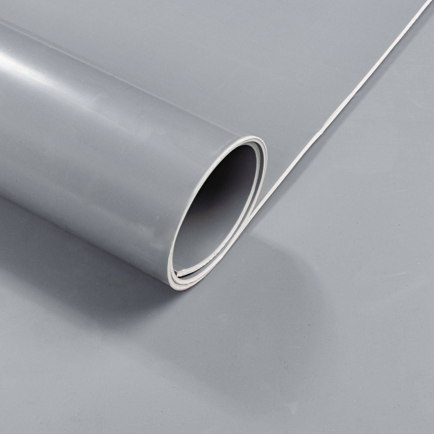 Nahaufnahme einer aufgerollten grauen, flexiblen Folie oder Vinylmatte auf einer grauen Oberfläche.