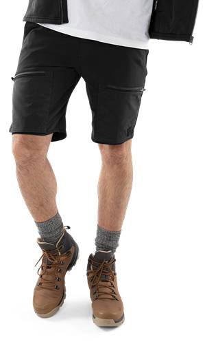 Eine Person trägt schwarze Cargoshorts, graue Socken und braune Schuhe und steht vor einem dunklen Hintergrund.