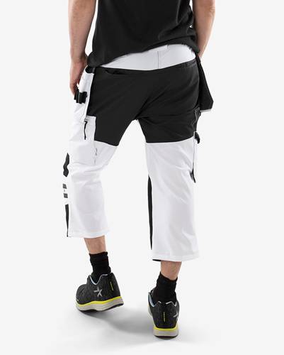 Person trägt schwarze und weiße Sportanzughose und Turnschuhe, geht von hinten zu sehen auf einem weißen Hintergrund.
