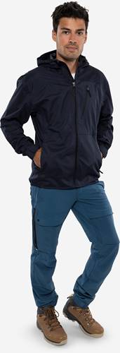 Eine Person in einer dunklen Jacke und blauen Hosen steht mit den Händen in den Taschen und vermittelt eine lässige, entspannte Körperhaltung.