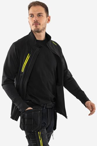 Eine Person trägt eine schwarze Jacke mit einem leuchtend gelben Reißverschluss und steht vor einem neutralen Hintergrund, wobei funktionale Kleidung präsentiert wird.