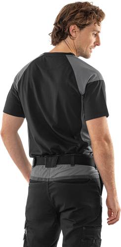 Eine Person in einem schwarz-grauen Kurzarmshirt und dunkler Hose wird von hinten gezeigt, mit herabhängenden Armen an den Seiten.