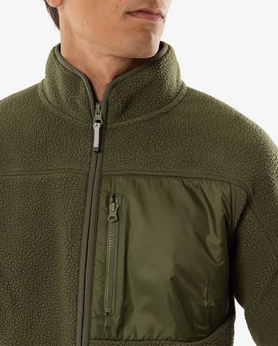 Eine Person trägt eine olivgrüne Fleecejacke mit einer Reißverschlusstasche auf der Brust, wobei die Textur und die praktischen Merkmale der Jacke hervorgehoben werden.