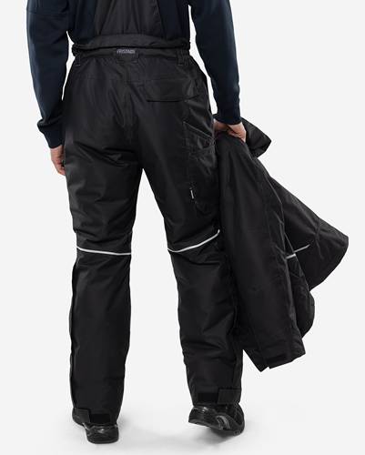 Eine Person in schwarzen Schneehosen und einer Jacke steht mit dem Rücken zur Kamera und hält eine weitere schwarze Jacke in der linken Hand.
