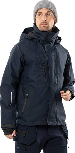 Eine Person, die eine dunkle, mit einer Kapuze versehene Winterjacke mit mehreren Reißverschlusstaschen trägt.