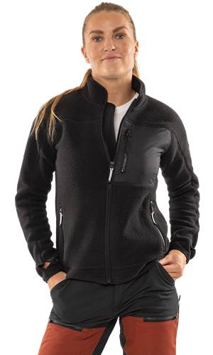 Eine Person, die eine schwarze Fleecejacke mit Reißverschluss trägt und die Hände in den Taschen hat, vor einem einfarbigen Hintergrund.